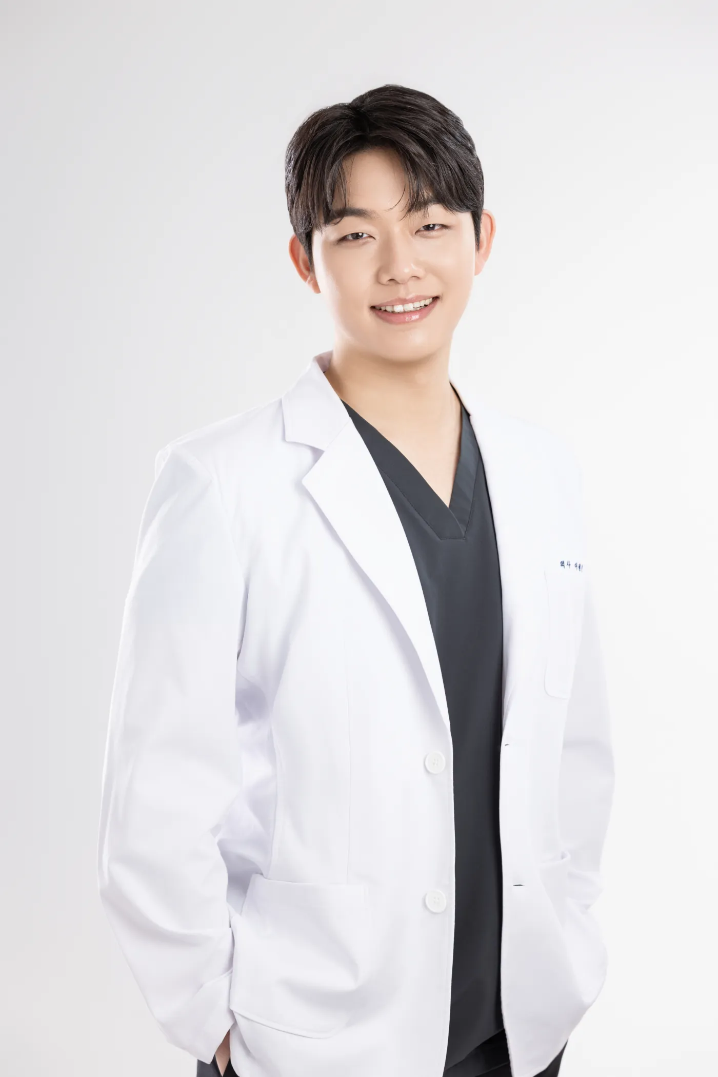 Dr. Lee Won Jin, representative director of Kind Global Clinic Myeongdong, in a white coat over dark scrubs.